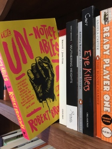 Image displays a row of books on a wooden shelf, with The Unnoticeables pulled out and hanging slightly off the edge. Other visible titles include Jane Eyre and Ready Player One.